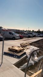 Sidewalk between parking lot with cars and dug out construction area.
