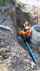 Orange jacket worker in whole doing underground pipe installation